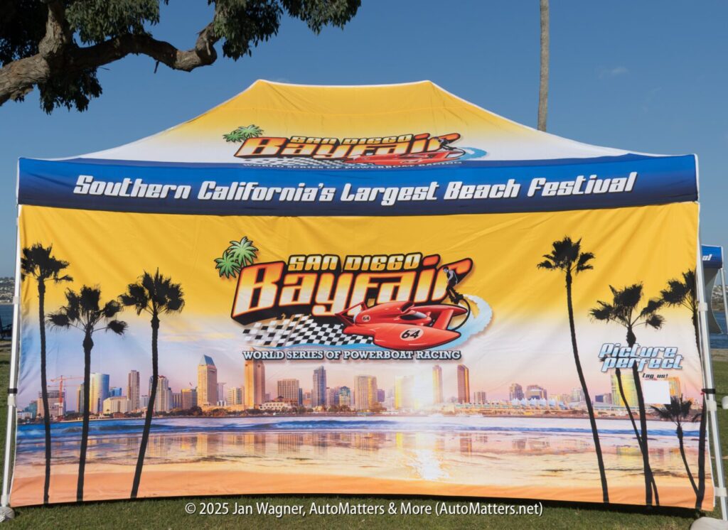 A yellow tent with "San Diego Bayfair" and "Southern California's Largest Beach Festival" printed, featuring a city skyline and palm trees in the background.