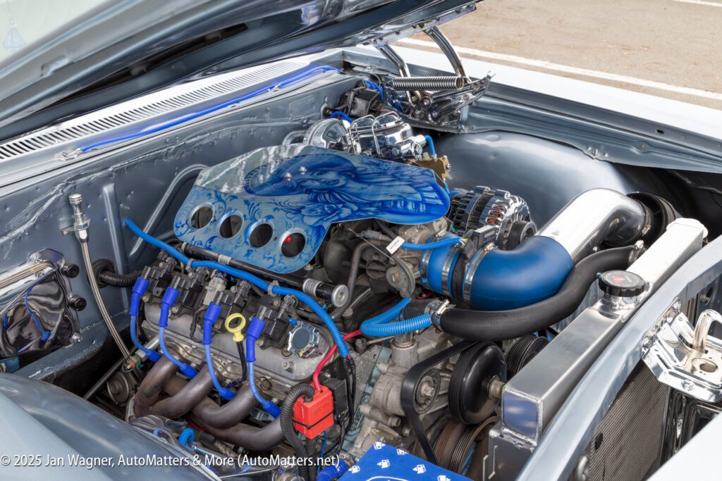 A detailed view of a modified car engine bay featuring blue accents, custom air intake, and intricate artwork on the engine cover.