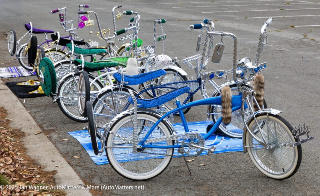 A row of customized lowrider bicycles with chrome parts and colorful seats are parked in an empty lot.