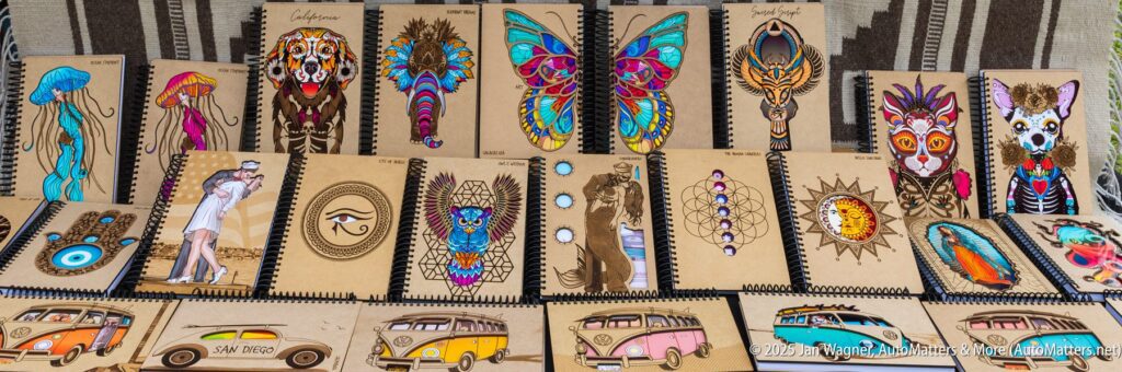 A display of spiral-bound sketchbooks with various colorful animal, vehicle, and geometric designs on their covers, arranged side by side on a table.