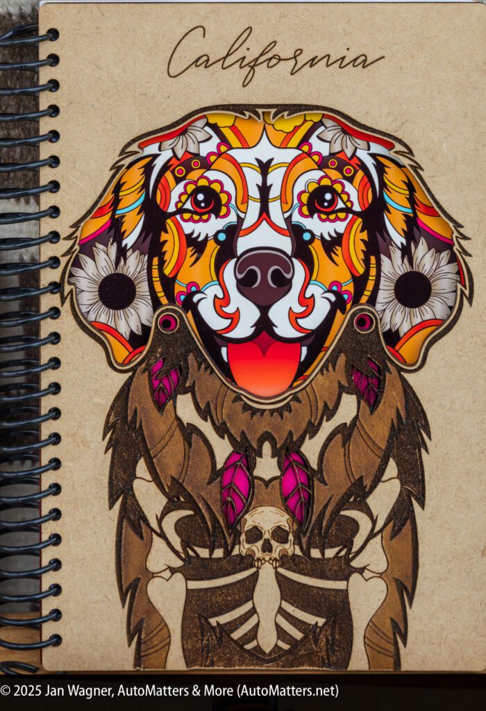 A spiral-bound notebook cover features a colorful, stylized dog with floral patterns and feathers, above a skeleton holding a skull, with "California" written at the top.