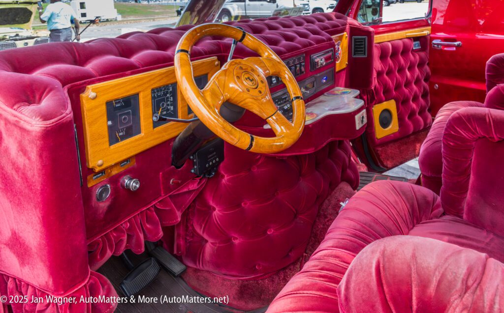 The interior of a car with plush, deep red velvet upholstery, a wooden dashboard, and a matching wood-trimmed steering wheel.