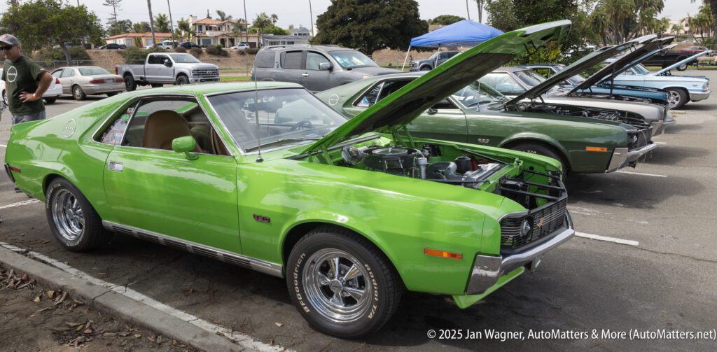 A row of classic cars with open hoods on display at an outdoor car show, featuring a bright green coupe in the foreground.