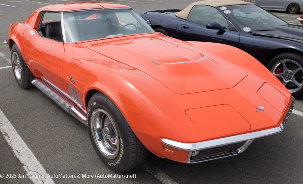 An orange classic Chevrolet Corvette Stingray parked in a lot next to a black convertible sports car.