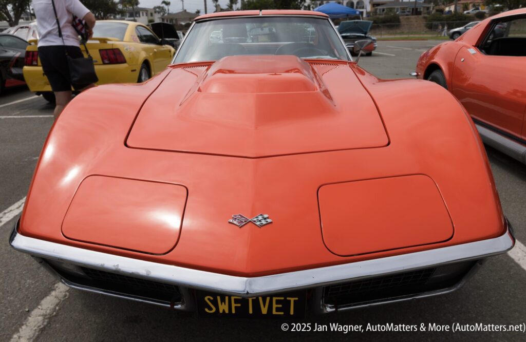 Front view of a classic orange Chevrolet Corvette parked outdoors at a car show, with a license plate reading "SWFTVET.