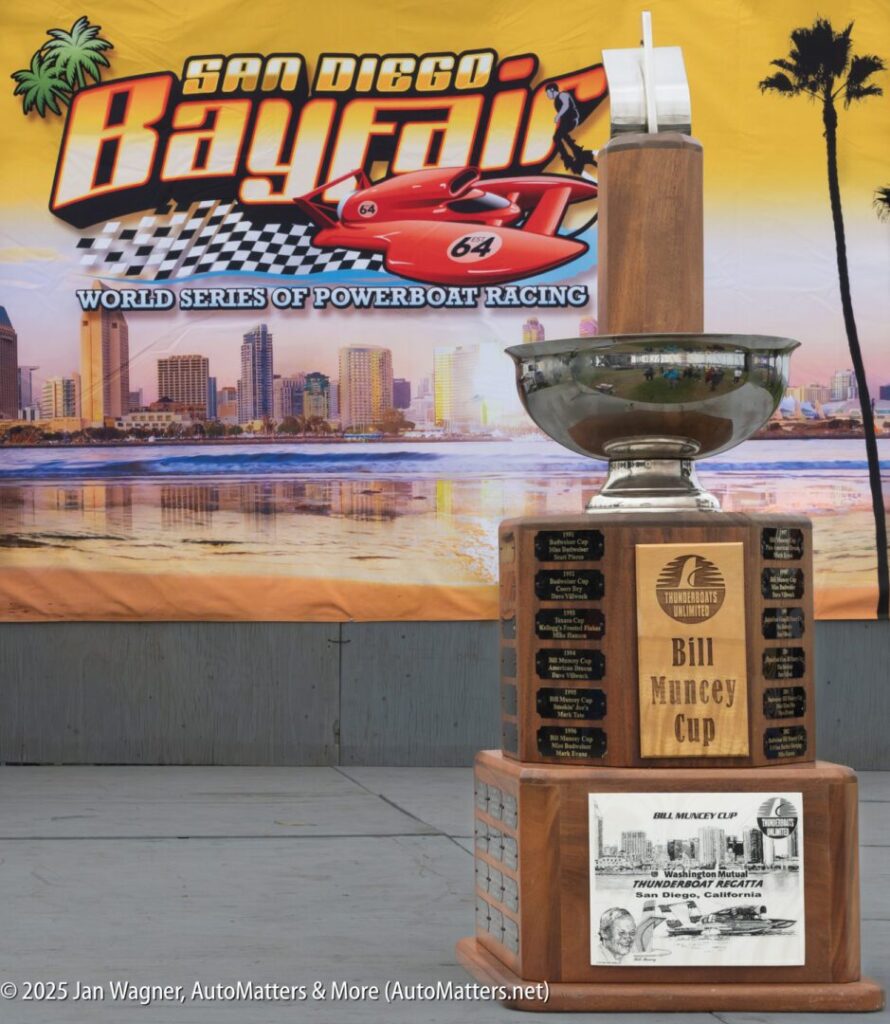 A large trophy labeled "Bill Muncey Cup" stands in front of a San Diego Bayfair powerboat racing banner, with a city skyline in the background.