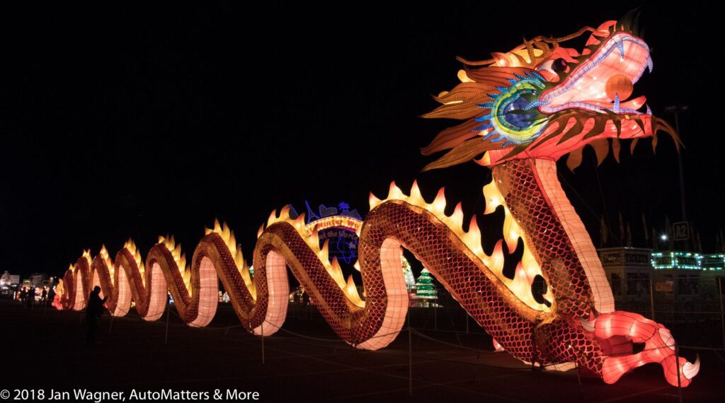 A large illuminated Chinese dragon lantern with vibrant colors and flame-shaped accents is displayed at night during a festival.
