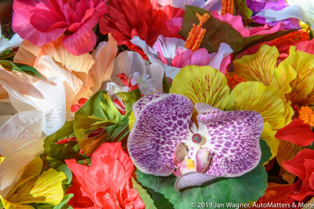 A close-up of various colorful artificial flowers, including a purple and white orchid in the center.