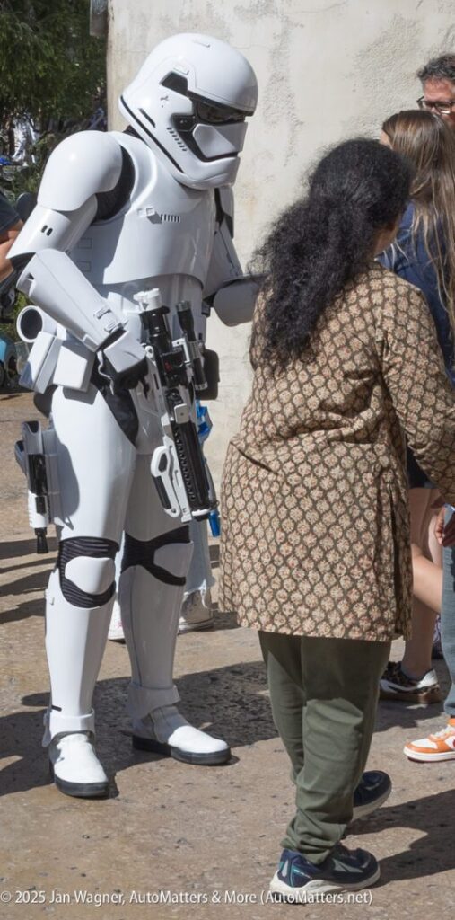 A person dressed as a Star Wars stormtrooper interacts with people outdoors near a wall.