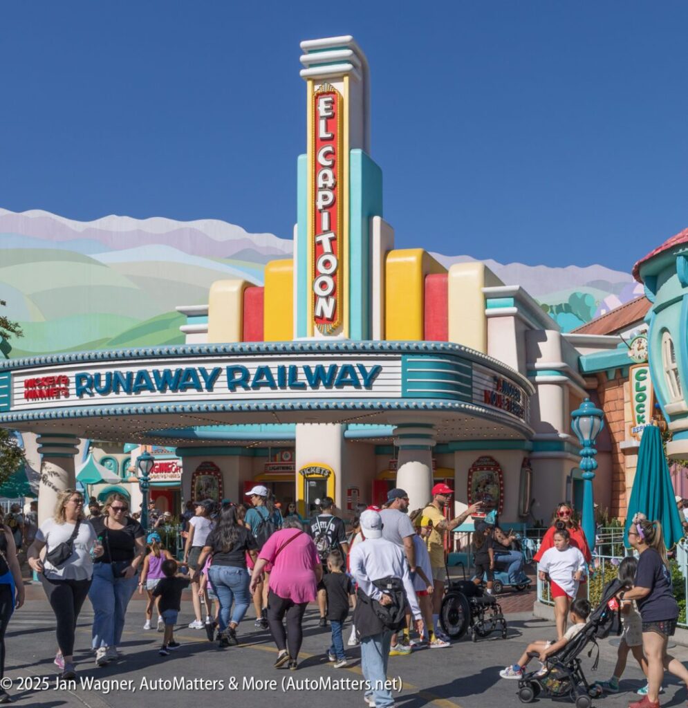 Crowds walk in front of the entrance to Mickey & Minnie's Runaway Railway at Disneyland, with a colorful El Capitoon Theater marquee and clear blue sky.