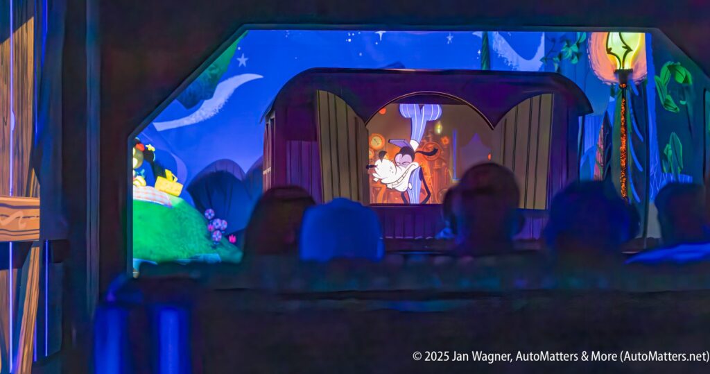 Animated scene featuring a skunk performing on a stage inside a colorful, whimsical setting, viewed from the perspective of an audience in a dimly lit room.