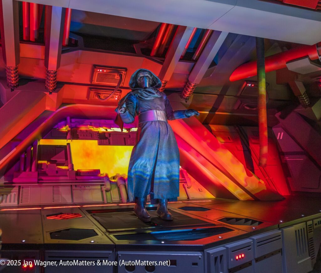 A person in a dark costume, resembling a sci-fi or Star Wars character, stands on a futuristic set with colorful lights and industrial details.