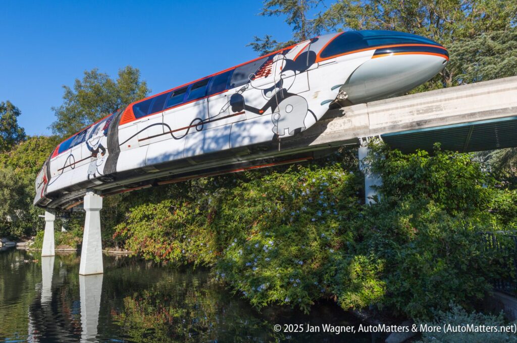 A monorail decorated with Star Wars characters travels on an elevated track above trees and a body of water.