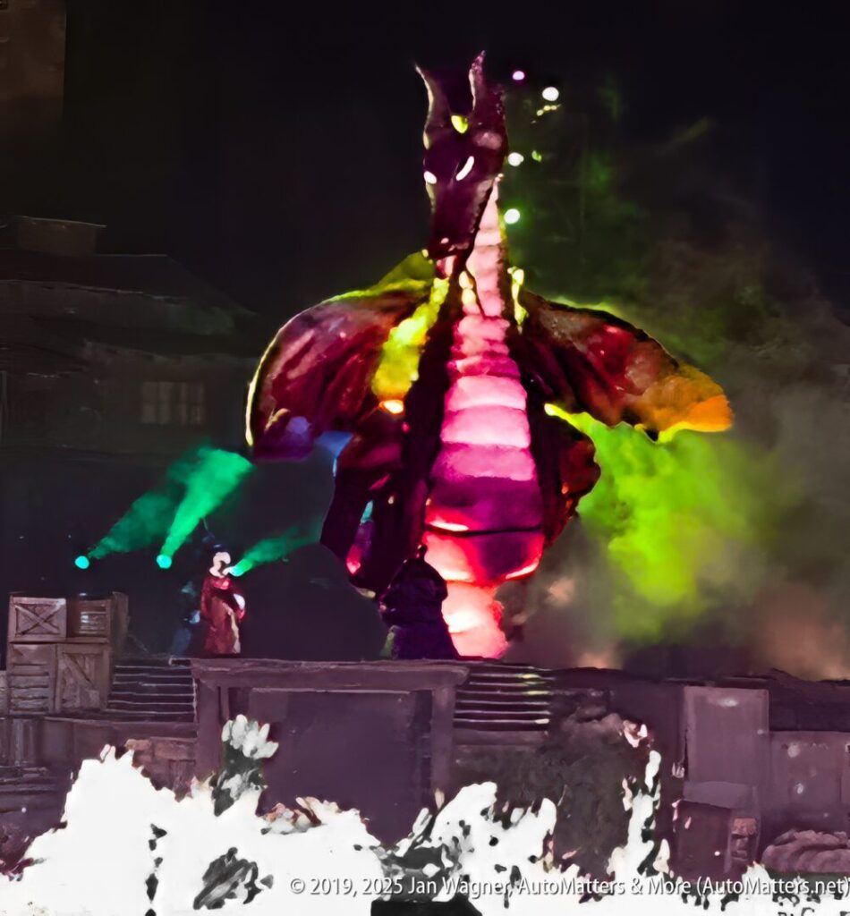 A large, illuminated dragon prop stands on stage with a performer nearby, surrounded by colored lights and stage effects.