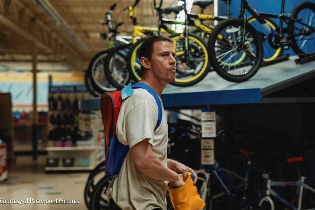 A man with a backpack stands in a store aisle, looking at bicycles displayed on racks.