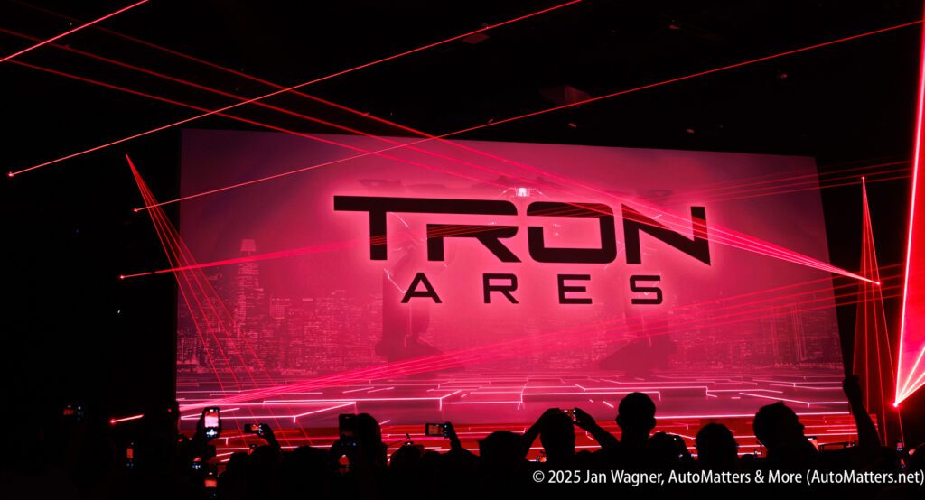 A large screen displays "TRON ARES" with red laser lights and silhouettes of an audience holding up phones.