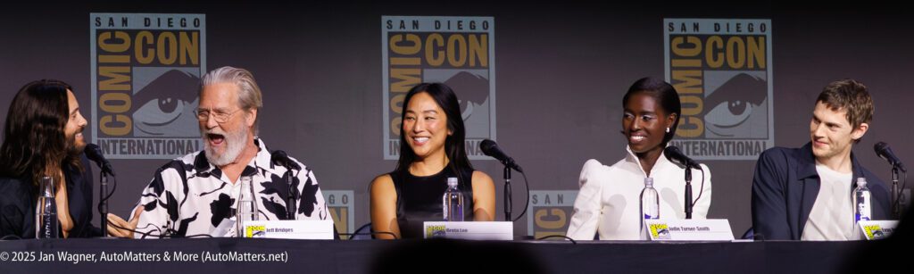 Five panelists sit at a Comic-Con International table, each with microphones, smiling and engaging with one another in front of Comic-Con banners.