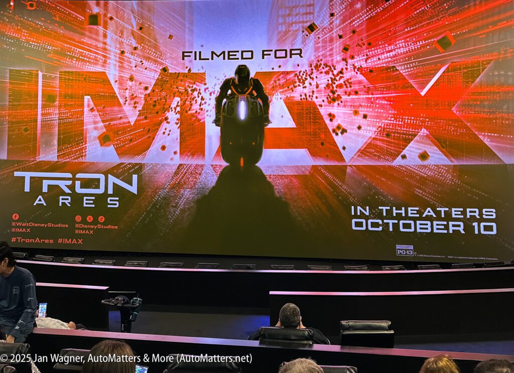 Large movie screen displays promotional image for "TRON: ARES," filmed for IMAX, with a release date of October 10. Theater seats and a few audience members visible in foreground.