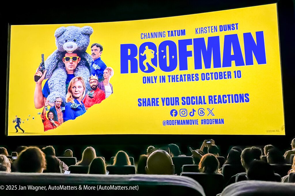 A movie theater audience views a bright yellow "ROOFMAN" film poster on screen, featuring actors, a man with a teddy bear, and social media links; release date is October 10.