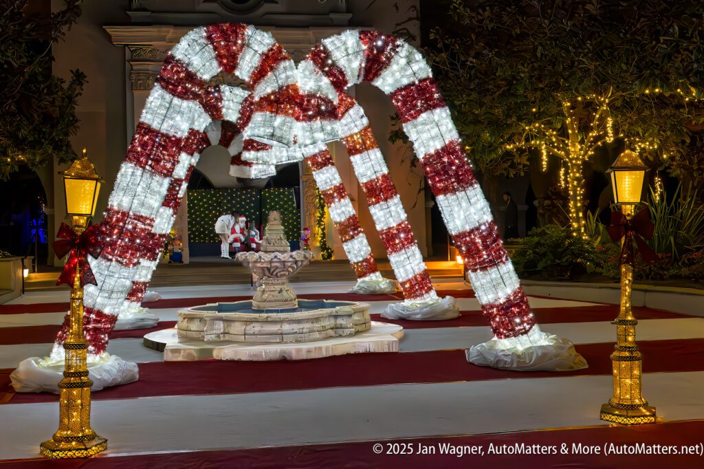 Large illuminated candy cane arches are displayed around a central fountain, with festive lights and decorations in the background at night.