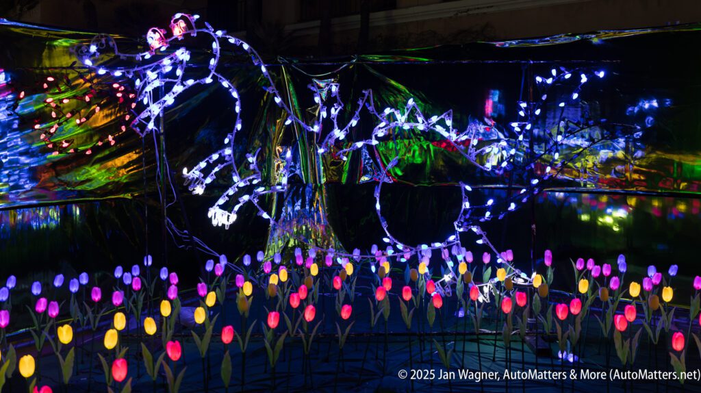 A dragon and two riders are outlined in purple string lights above a field of glowing, multicolored artificial tulips at night.