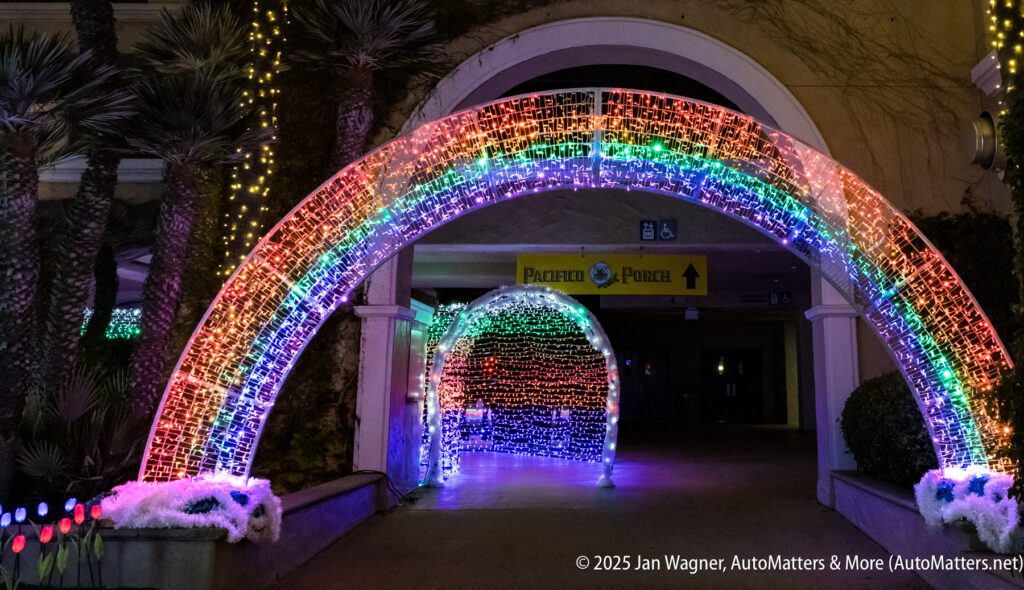 A brightly lit archway with rainbow-colored lights leads to another illuminated tunnel outside a building at night.