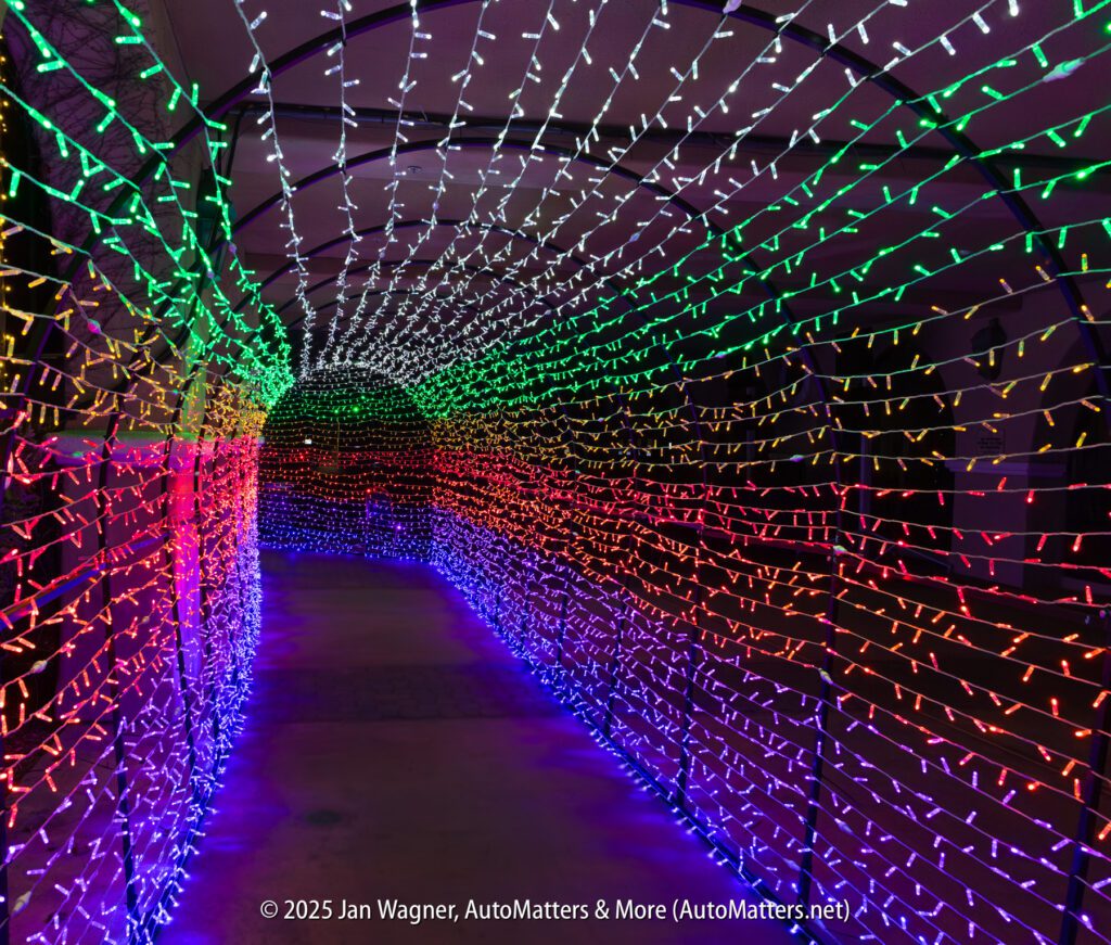 A tunnel walkway is covered in rows of colorful LED holiday lights forming a rainbow pattern overhead and along the sides.