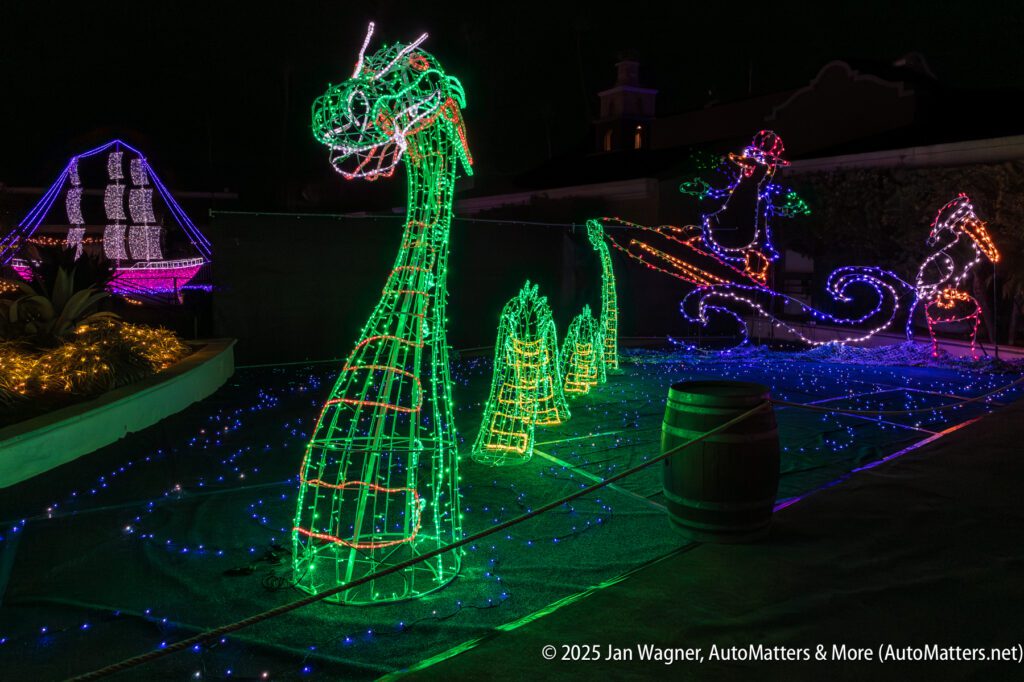 Colorful holiday light sculptures feature a green sea serpent, a sailing ship, and a penguin on a sleigh, all displayed on a rooftop at night.