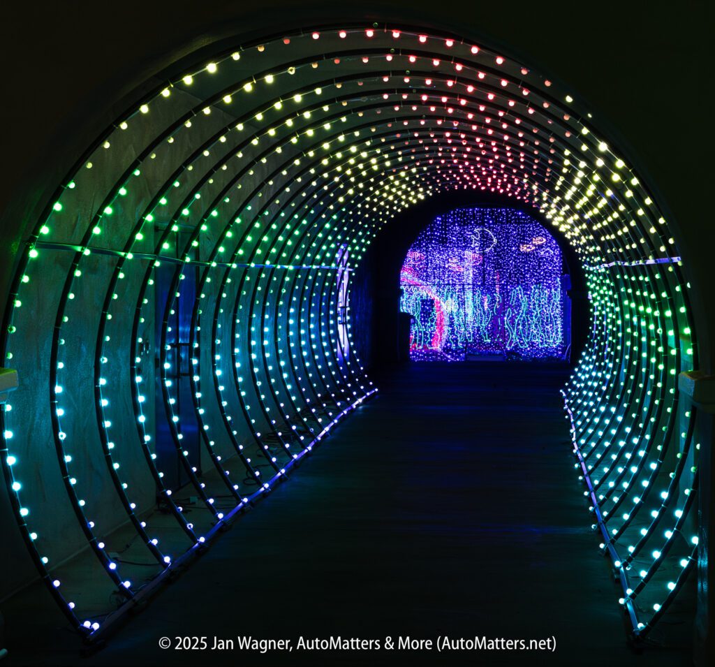A tunnel with curved arches is lit by rows of multicolored LED lights, leading to a vibrant display of lights in the distance.