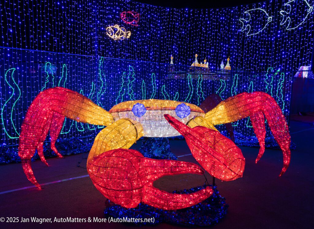 Large illuminated crab sculpture with red claws and yellow body, surrounded by blue, undersea-themed decorative lights and fish shapes in the background.