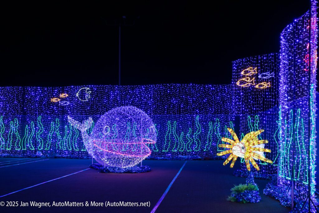 A display of blue, yellow, and white lights forms an underwater scene with a whale, fish, seaweed, and a sun or pufferfish on a dark background.