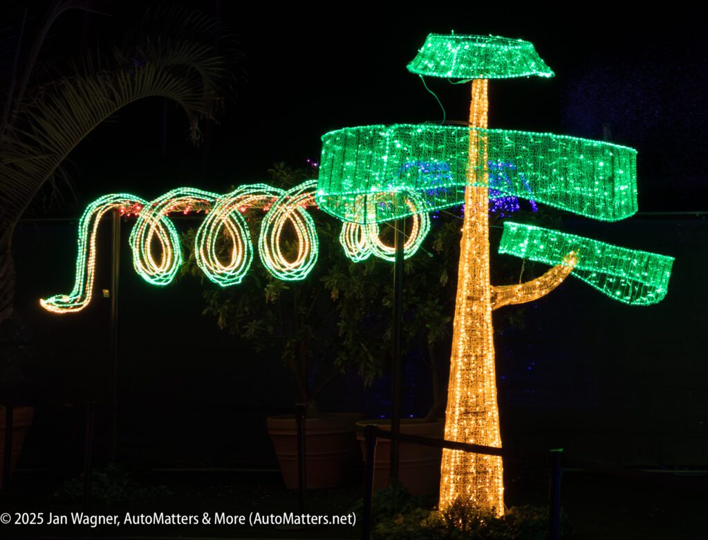 A tree and a long, winding shape are outlined with green and yellow holiday lights, illuminated at night.