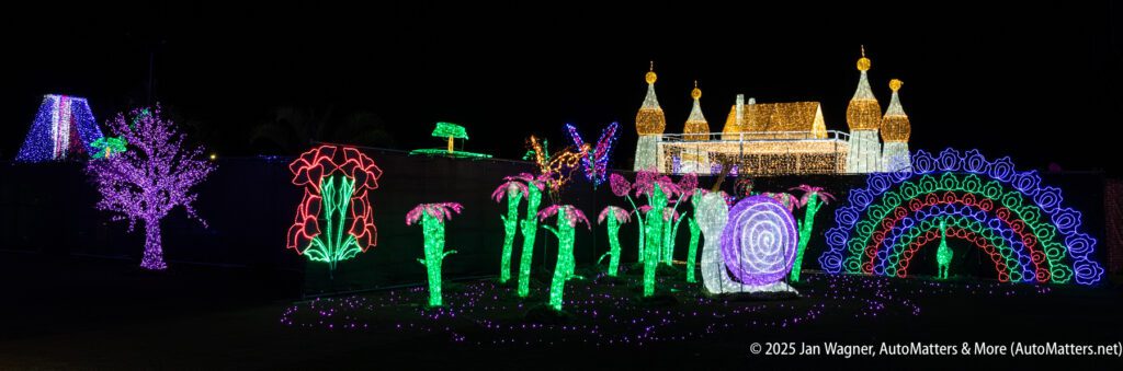 A nighttime scene displays colorful holiday light sculptures, including trees, mushrooms, a castle, a peacock, and a rainbow, all illuminated against a dark background.