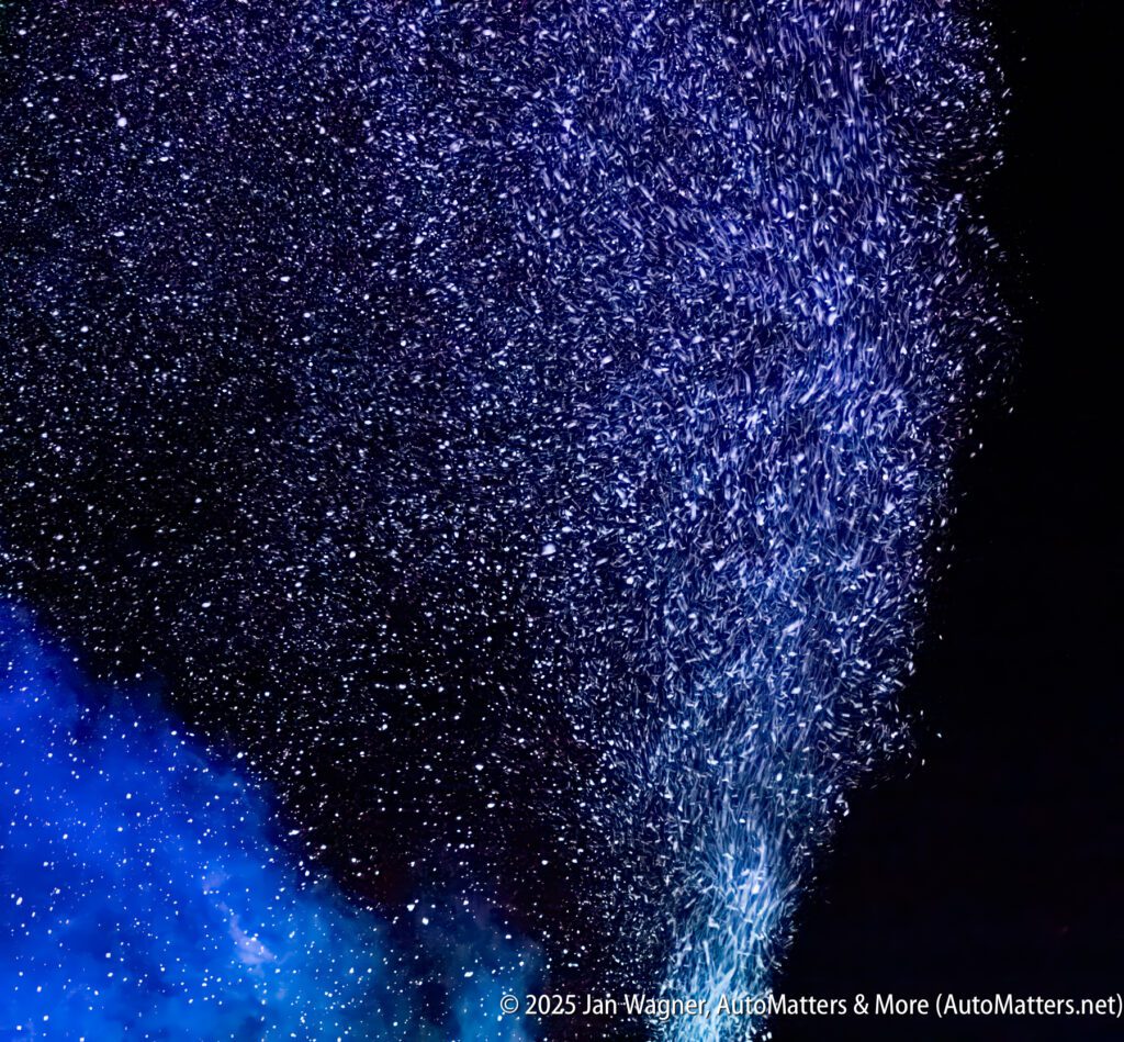 A dense shower of tiny water droplets or particles illuminated by blue and purple light against a dark background.