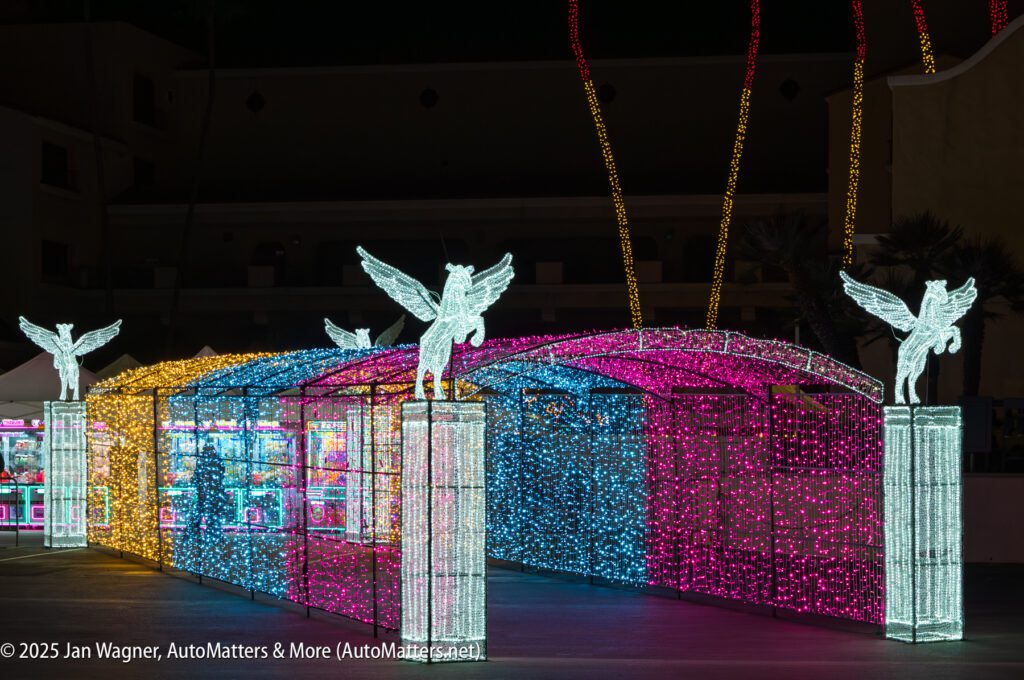 A tunnel covered in colorful LED lights with illuminated winged horse statues on columns at the entrance, photographed at night.