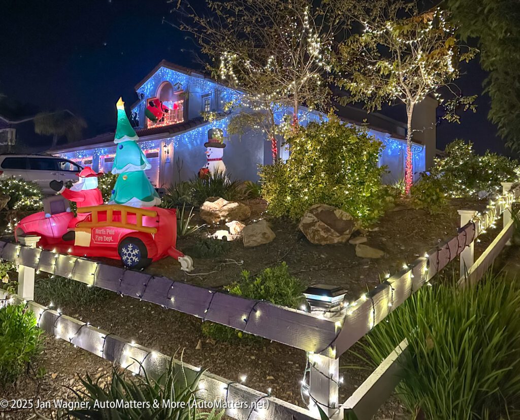 A house decorated with Christmas lights, featuring inflatable holiday figures including a fire truck with a Christmas tree and Santa on the roof.