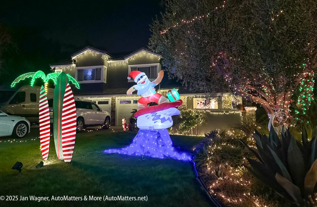 Front yard with Christmas lights, inflatable Santa on a surfboard, two striped palm tree decorations, and a house decorated with string lights at night.