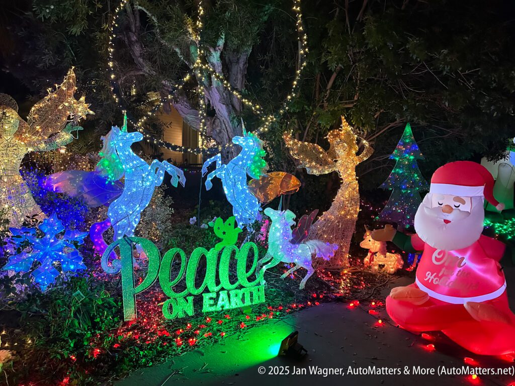 Christmas yard display at night with lighted unicorns, deer, a "Peace on Earth" sign, and an inflatable Santa Claus.