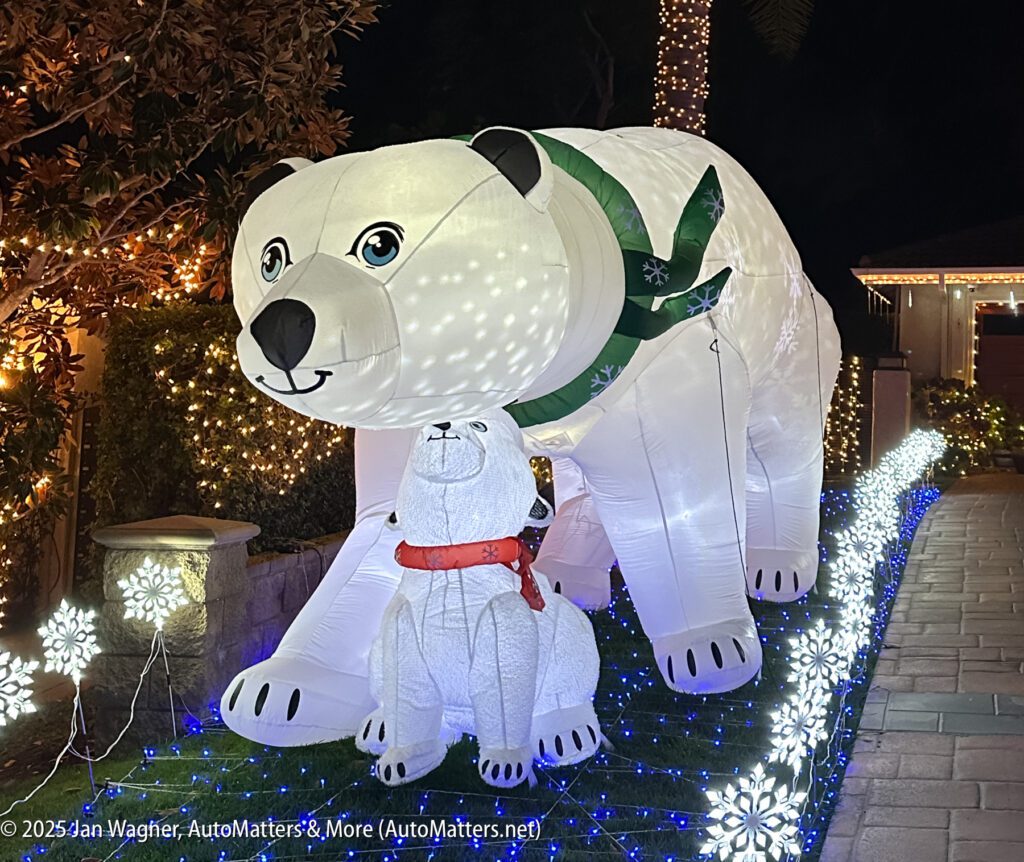 Large outdoor inflatable decorations of a polar bear and a smaller bear with a red scarf are displayed in a yard, surrounded by illuminated snowflake lights at night.