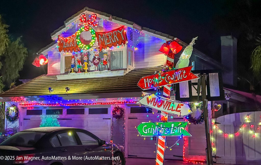 House decorated with colorful Christmas lights, a "Merry Merry" sign, cartoon cutouts, and festive signposts pointing to "Home Sweet," "Whoville," and "Gingrsted." A car is parked in front.