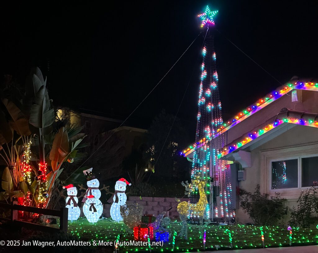A house decorated with colorful Christmas lights, featuring three illuminated snowmen, two reindeer, and a tall tree-shaped light display with a star on top.