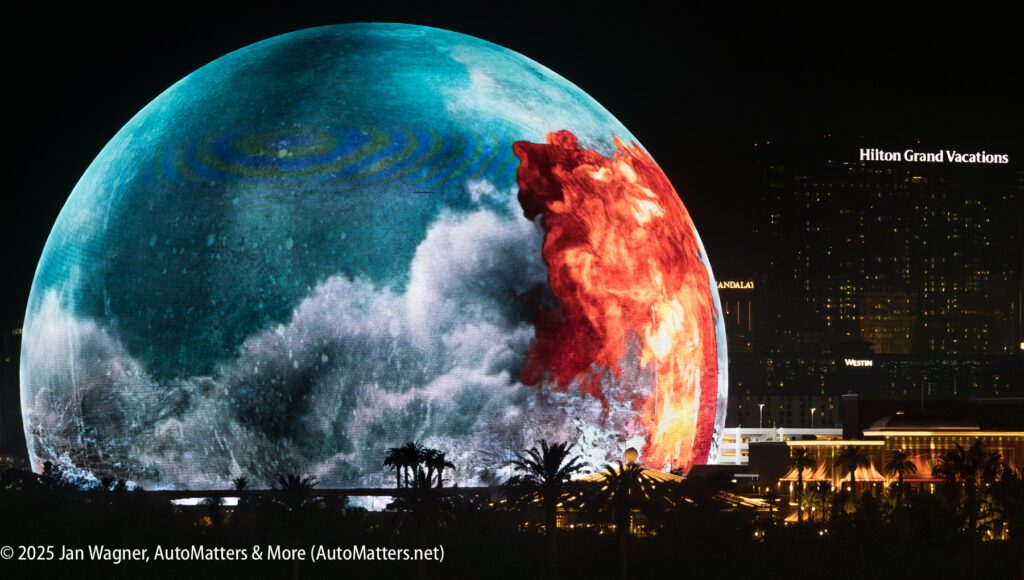 A large spherical LED screen displays vivid ocean and fire visuals at night, with city buildings and the Hilton Grand Vacations sign visible in the background.