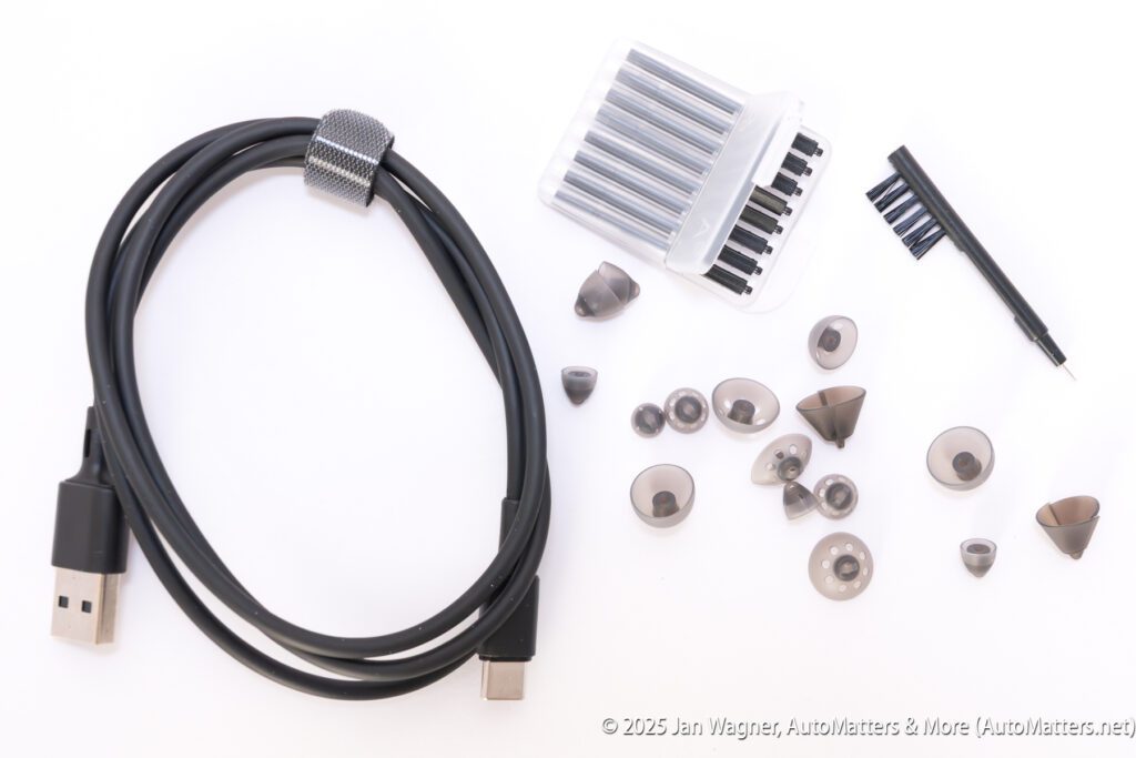 A USB-C to USB-A cable, various screwdriver bits, a cleaning brush, a screwdriver handle, and multiple silicone earbud tips are arranged on a white surface.