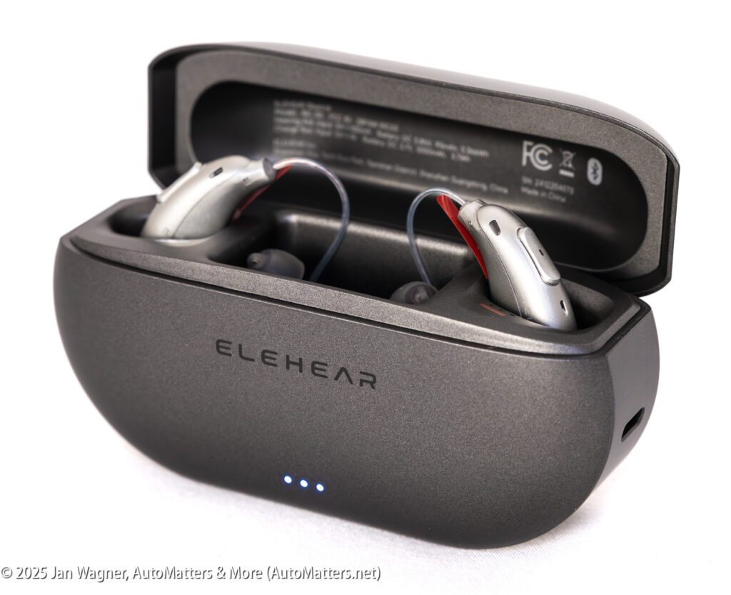 A pair of ELEHEAR hearing aids rest in their open charging case, which displays indicator lights and product details on the inside lid.