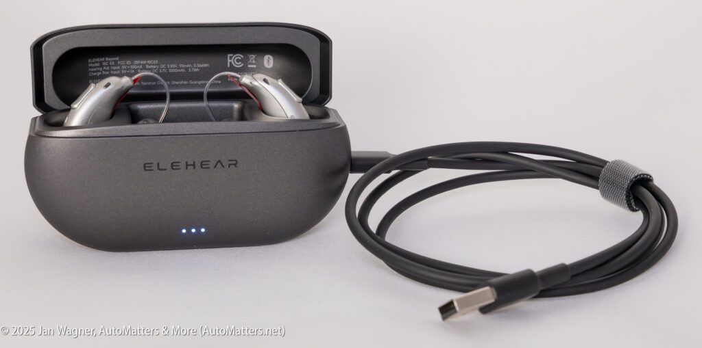 ELEHEAR hearing aids resting in an open charging case, with a USB-C charging cable placed beside the case.