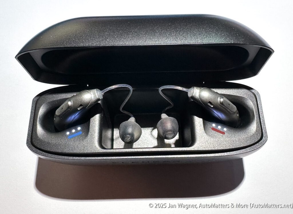A pair of wireless earbuds with ear hooks are placed in a black charging case, with blue and red markings indicating left and right sides.