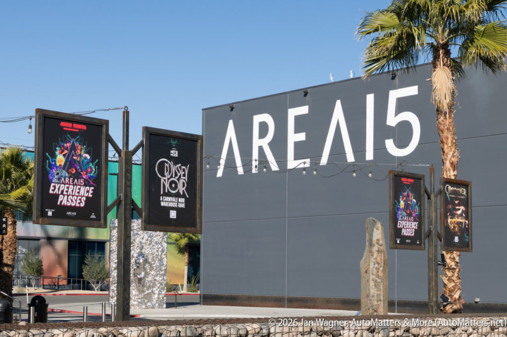 The exterior of AREA15 with large white signage and palm trees, featuring posters advertising events and experience passes.