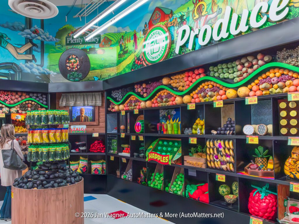 Colorful supermarket produce section display with neatly arranged fruits and vegetables on shelves; a few shoppers are present, and the wall is painted with food-themed murals.
