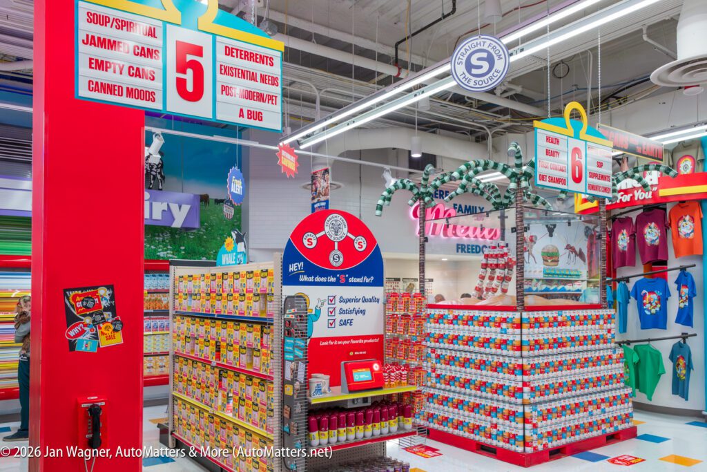 Colorful grocery store display with canned goods, detergent, and holiday decorations; signs feature playful product categories and a red information kiosk stands in the center.