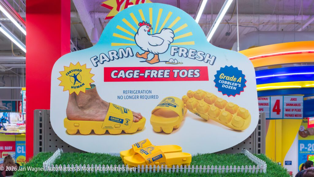 Display sign features "Farm Fresh Cage-Free Toes" sandals shaped like egg cartons, with a cartoon chicken and product samples shown below on a store shelf.